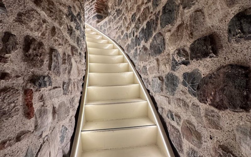 Curved stone tunnel with illuminated white stairs leading upward.