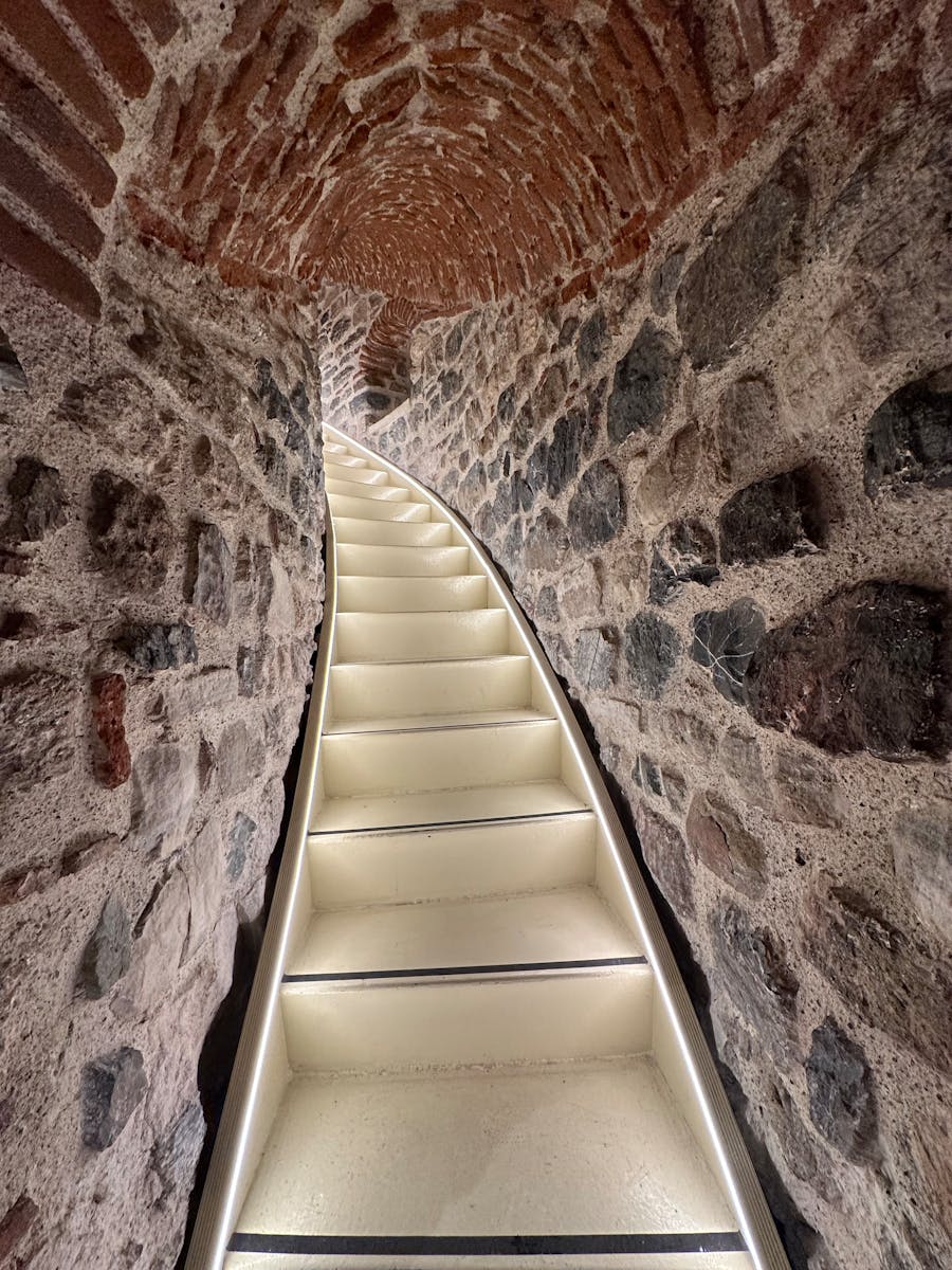 Curved stone tunnel with illuminated white stairs leading upward.